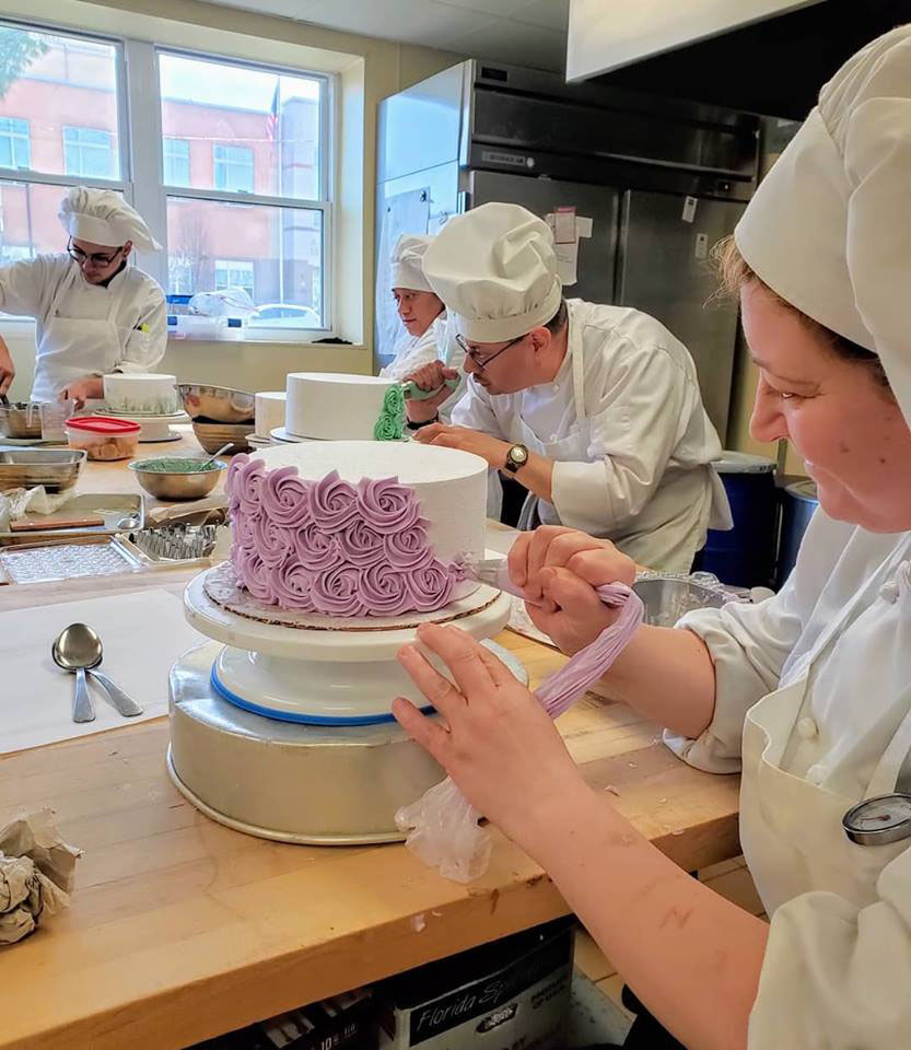 Chefs decorating a cake with icing.