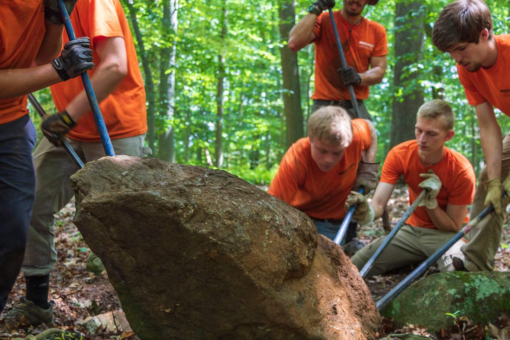 Members of the Middlesex County Conservation Corps working on moving a boulder.